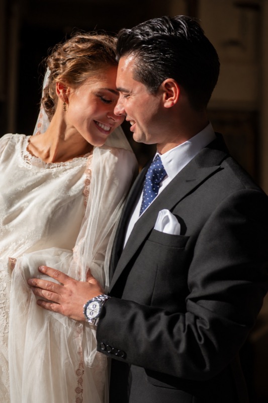 Los novios abrazados y sonriendo, iluminados por un haz de luz lateral