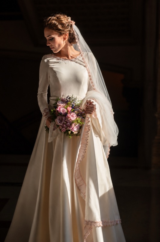 Novia con mantilla y ramo, retratada con luz de ventana antes de la ceremonia