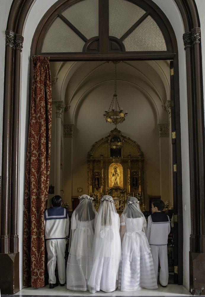 Cinco niños de comunión de espaldas ante el retablo dorado de una parroquia de Sevilla