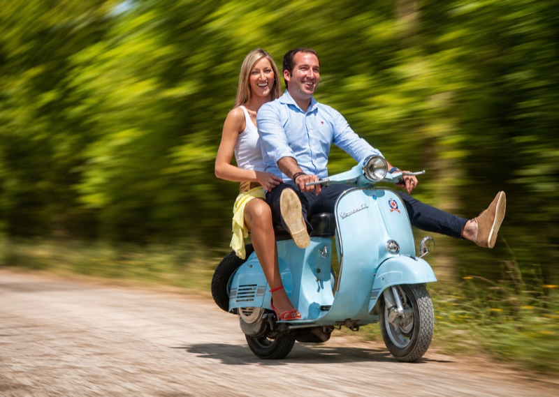 Pareja en una Vespa celeste en marcha por un camino de tierra